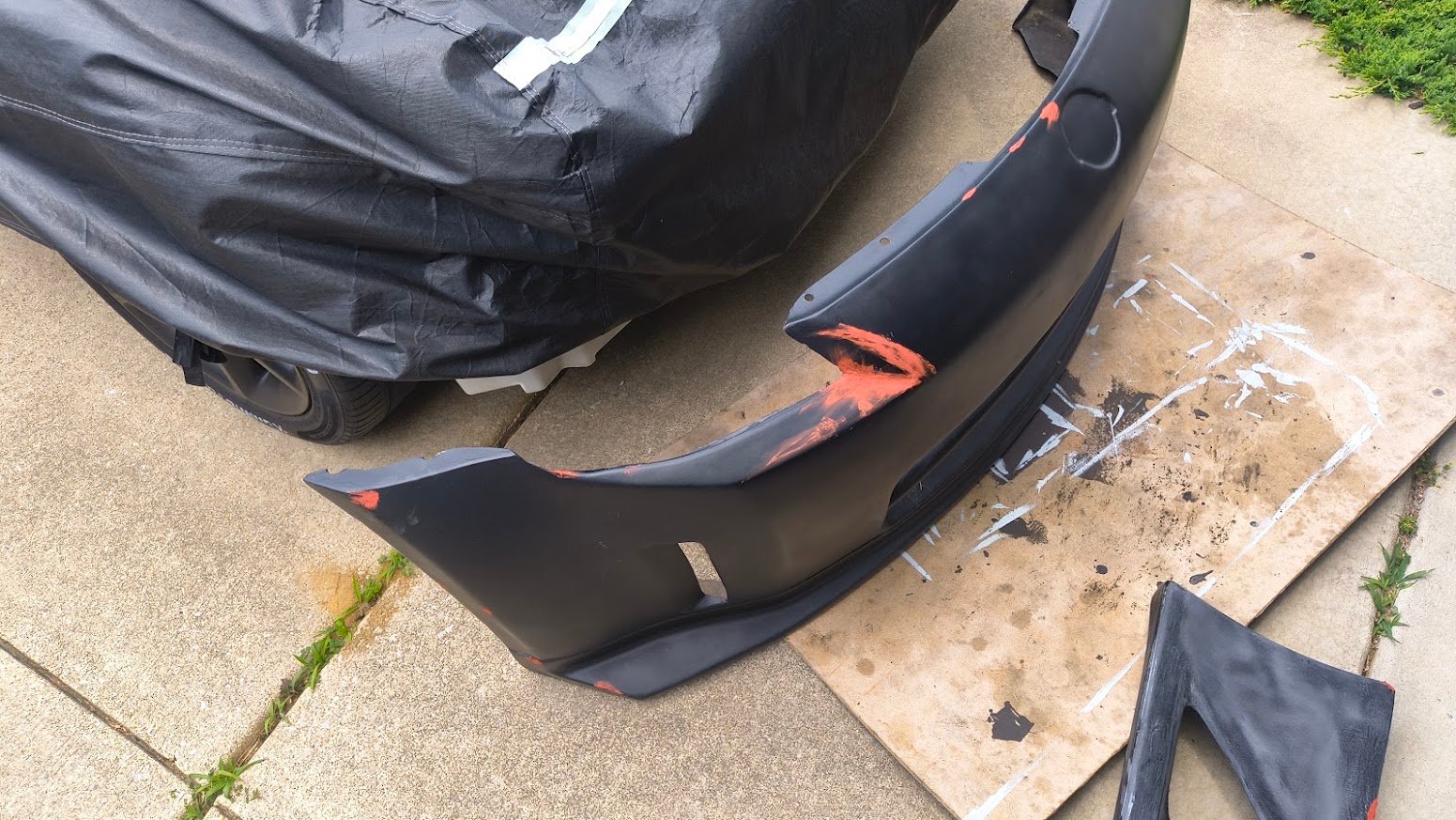 Fiberglass automotive bumper being repaired beside a covered project car